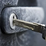 Ключ вставлен в покрытый инеем замок двери автомобиля